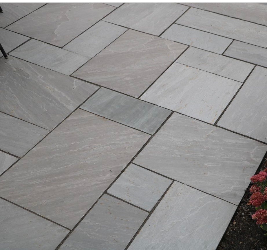 Gray stone tiles are arranged in a geometric pattern on a patio. Red flowers are visible on the right edge.
