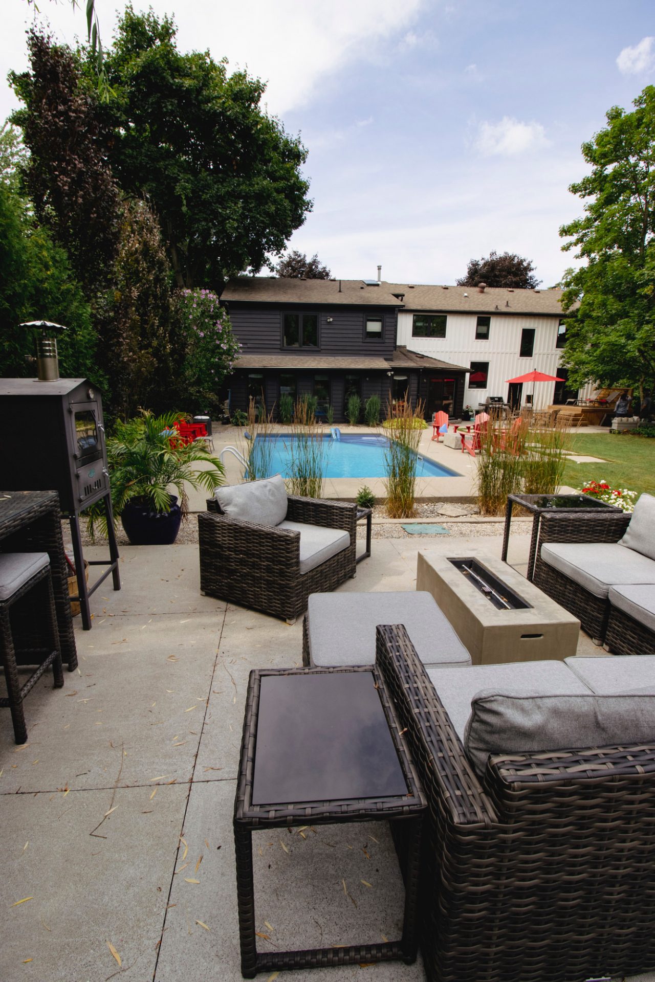 Modern backyard with a swimming pool, wicker furniture, and a two-tone house. Trees and a patio area complete the relaxing outdoor setting.