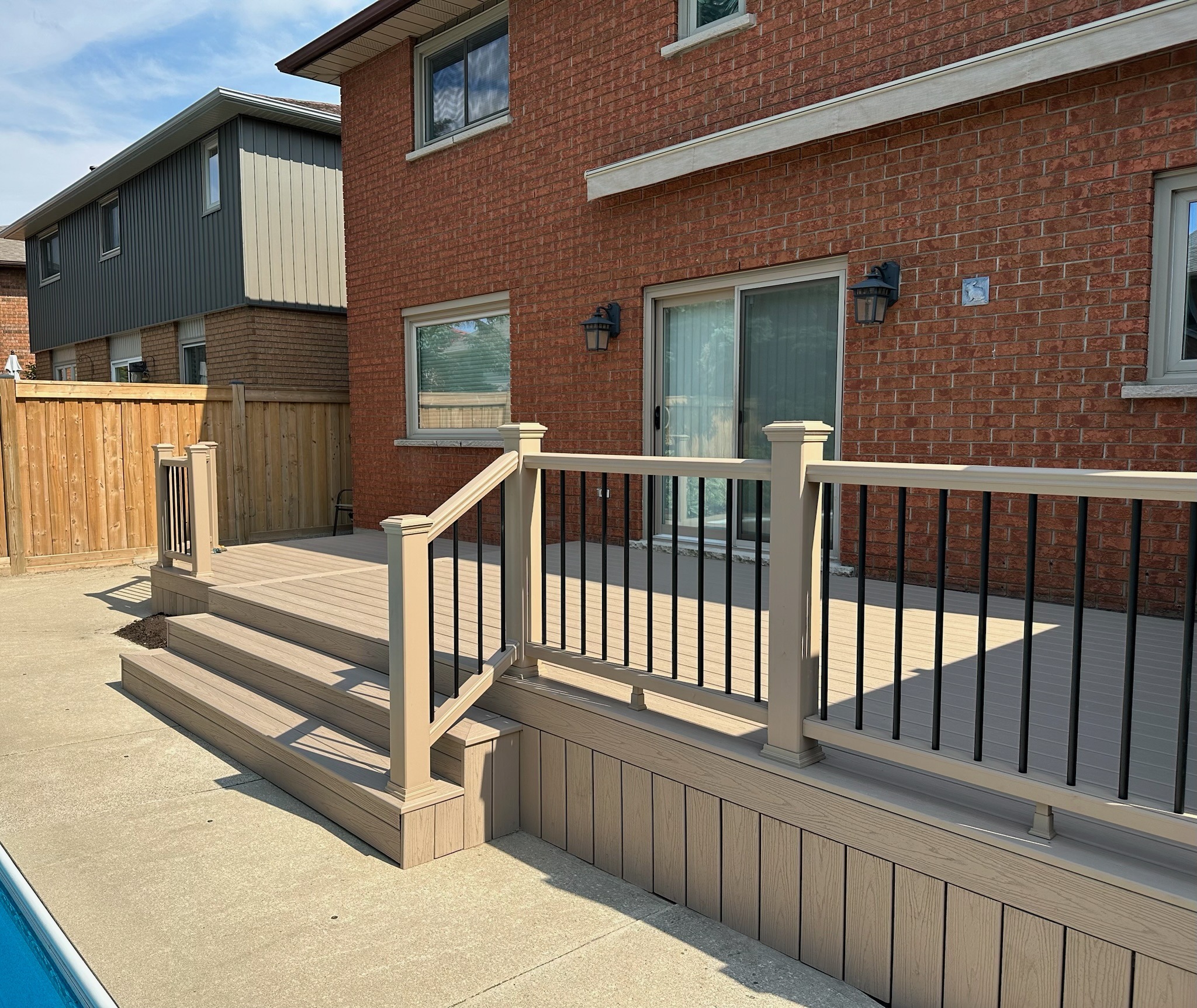 Brick house with a wooden deck and steps, bordered by a wooden fence. No recognizable landmarks or historical buildings are visible.