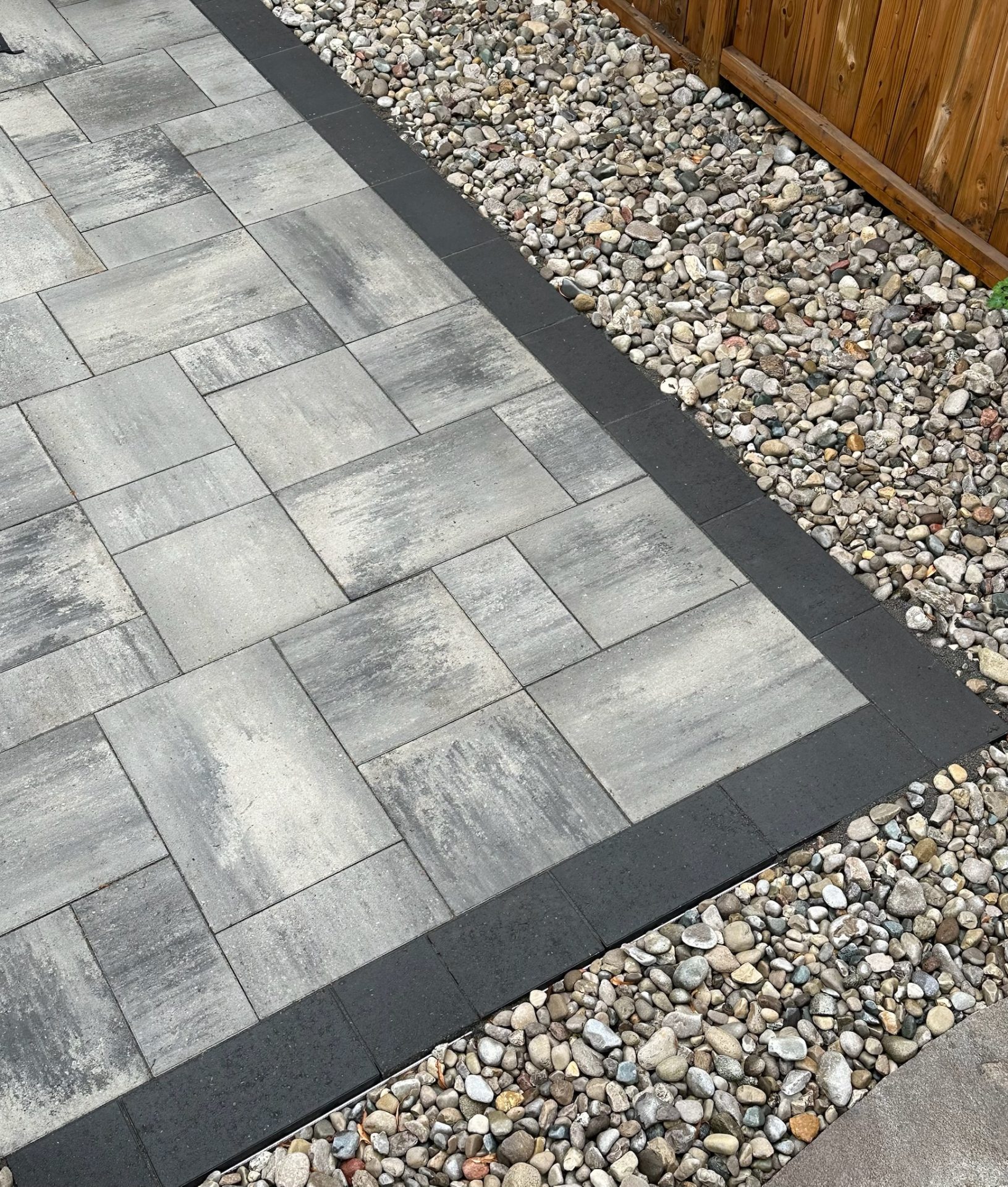 A paved path with gray tiles bordered by rocks and a wooden fence, creating a neat and modern outdoor space.