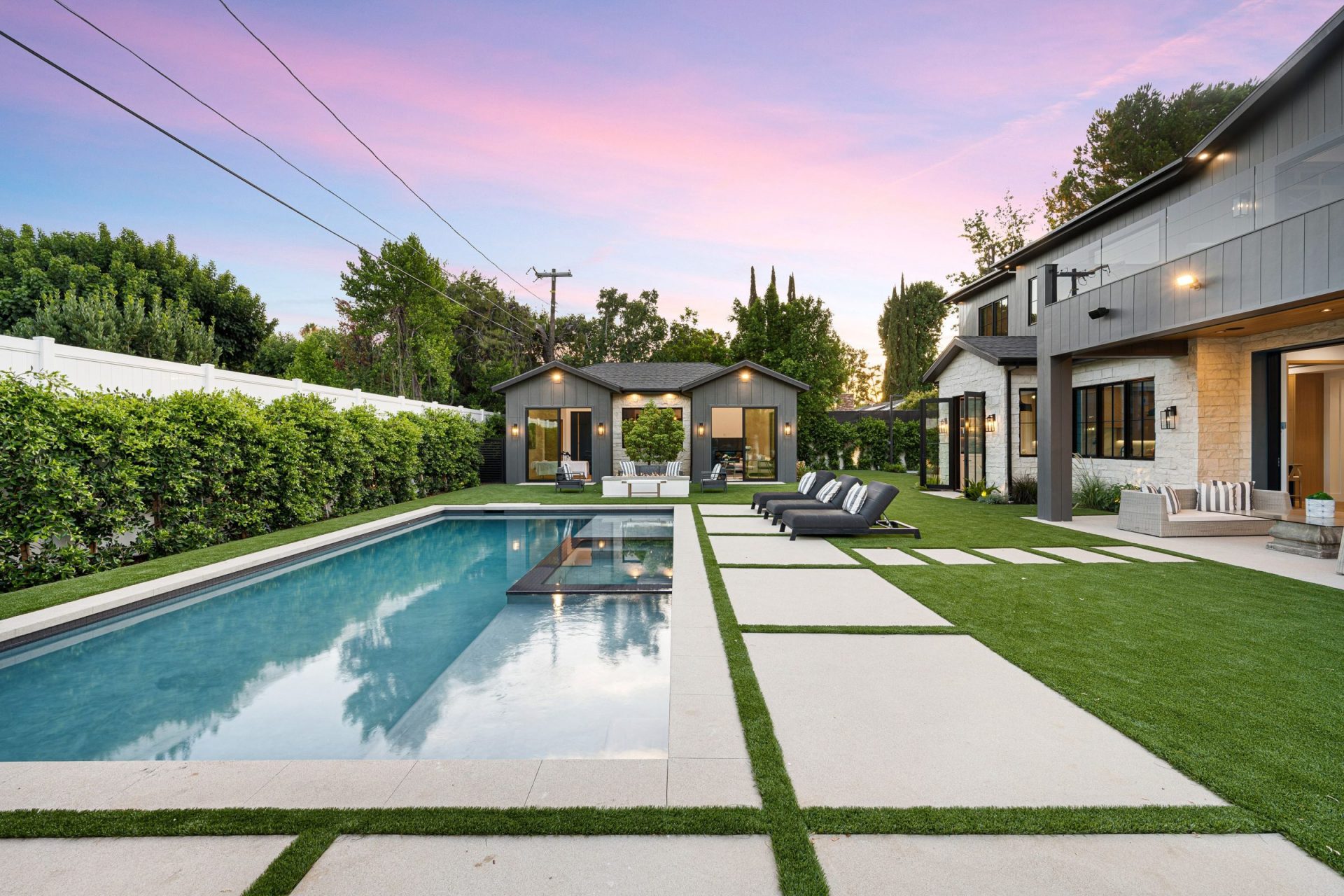 Modern backyard with a sleek swimming pool, lounge chairs, and well-manicured lawn. Contemporary house features large windows and minimalistic design.