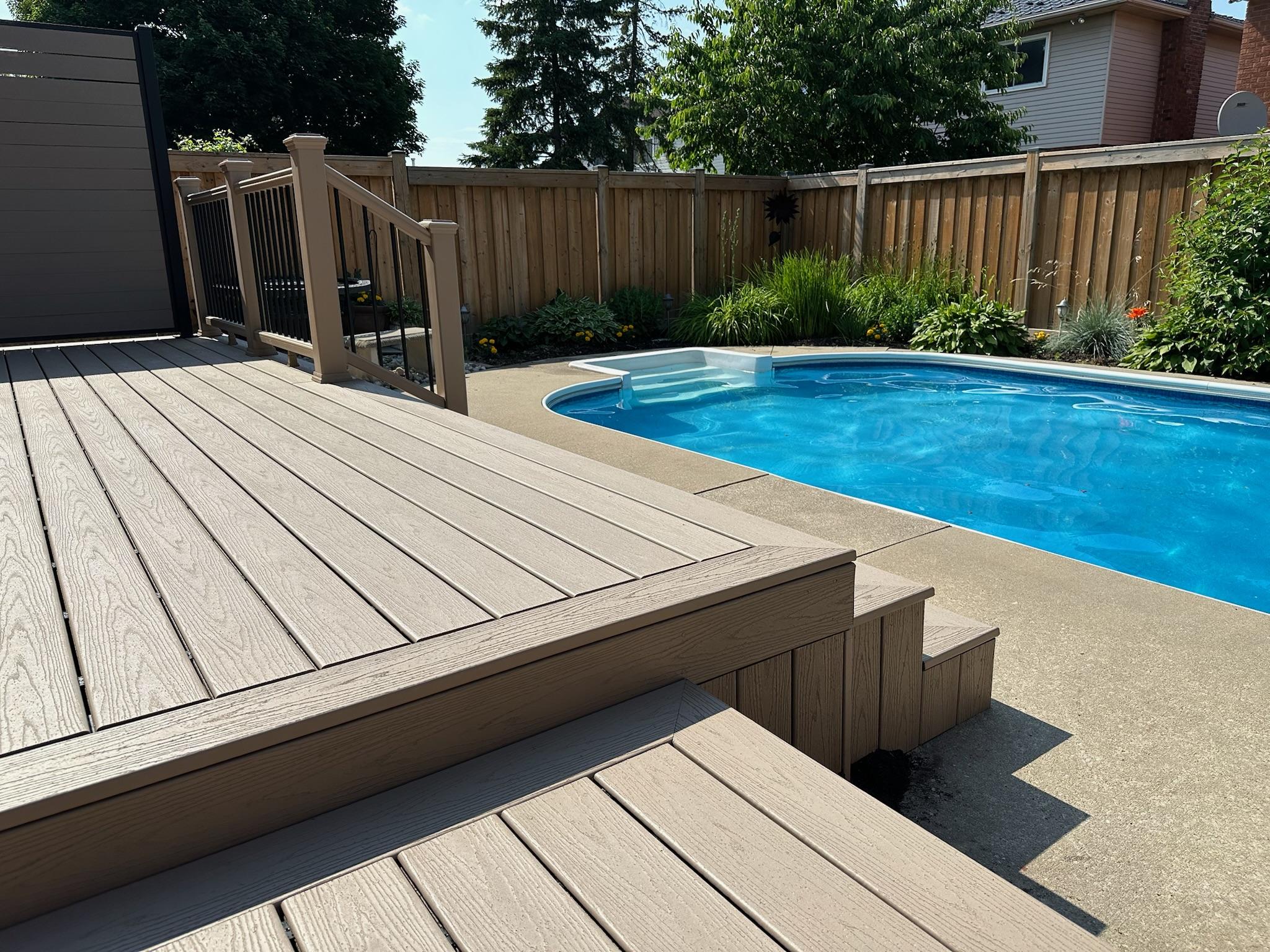 A composite deck with built-in steps overlooking a backyard pool, surrounded by wooden fencing and lush landscaping.