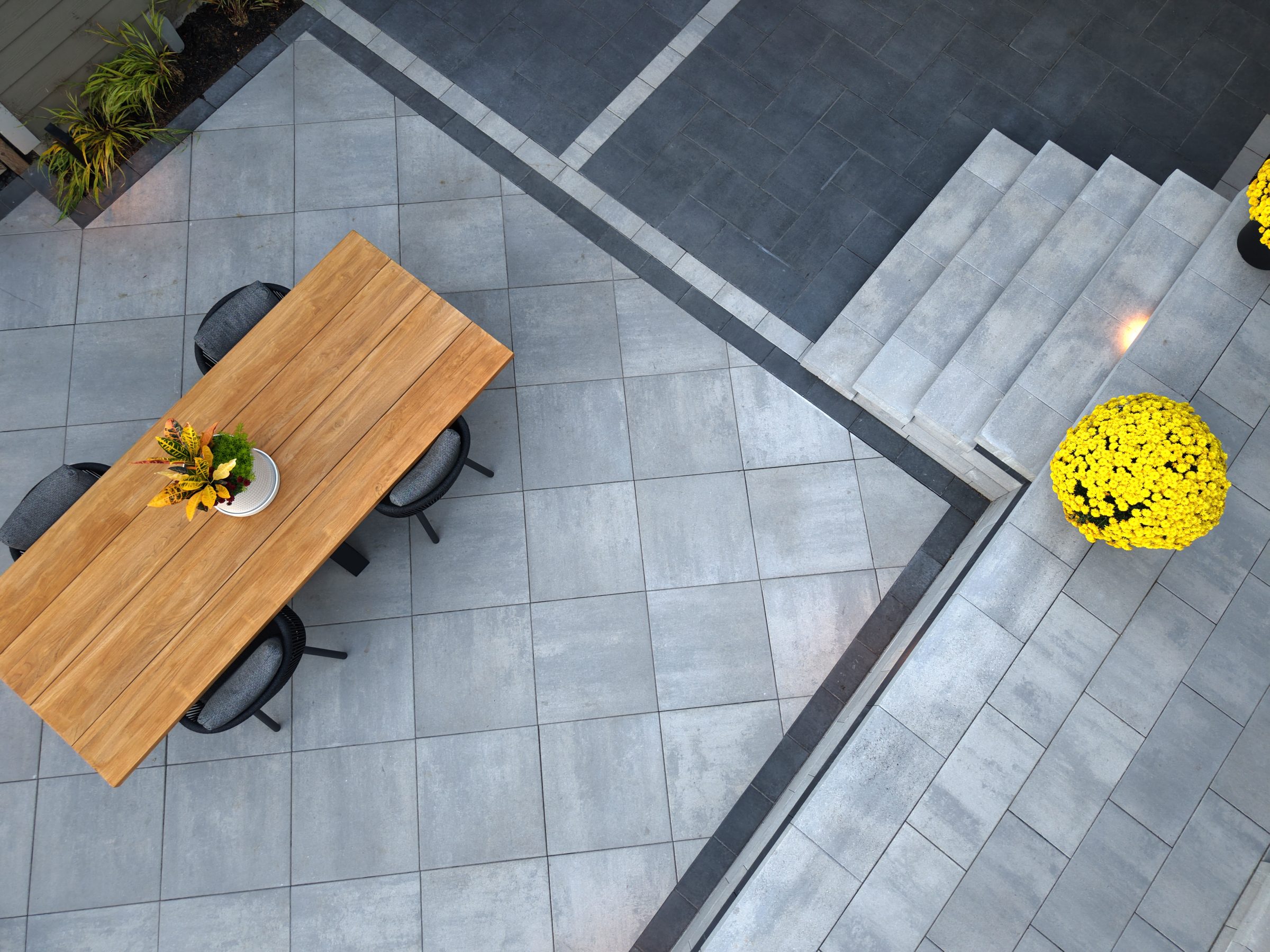 High-angle shot of light grey square pavers meeting dark grey stone steps with yellow flower pots providing a pop of color.