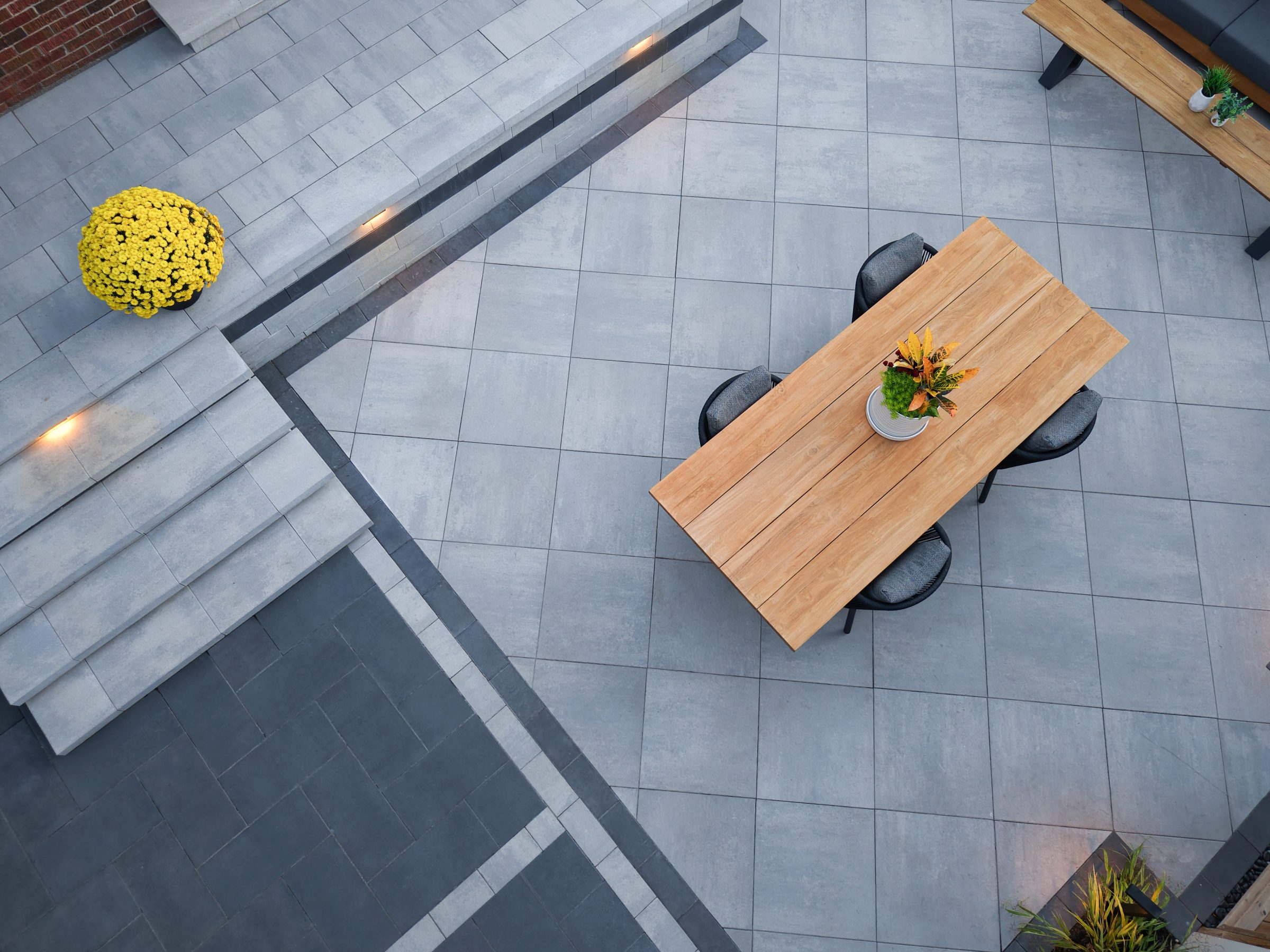 Aerial view of a natural wood dining table centered on light grey Molina patio stones with dark perimeter accents.
