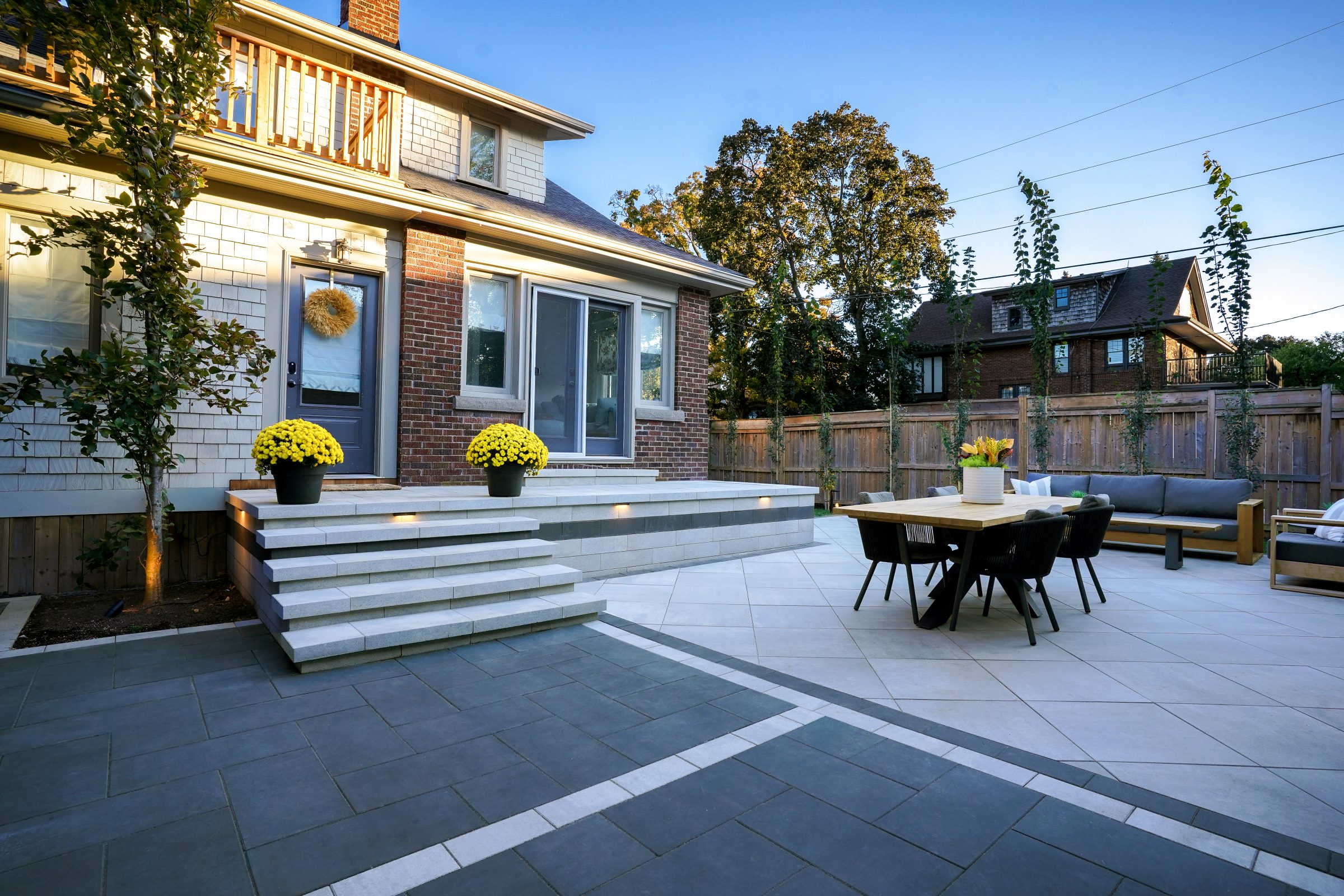 Large outdoor patio with a wooden dining table, black woven chairs, and a grey sectional sofa on Cloudburst stone pavers.