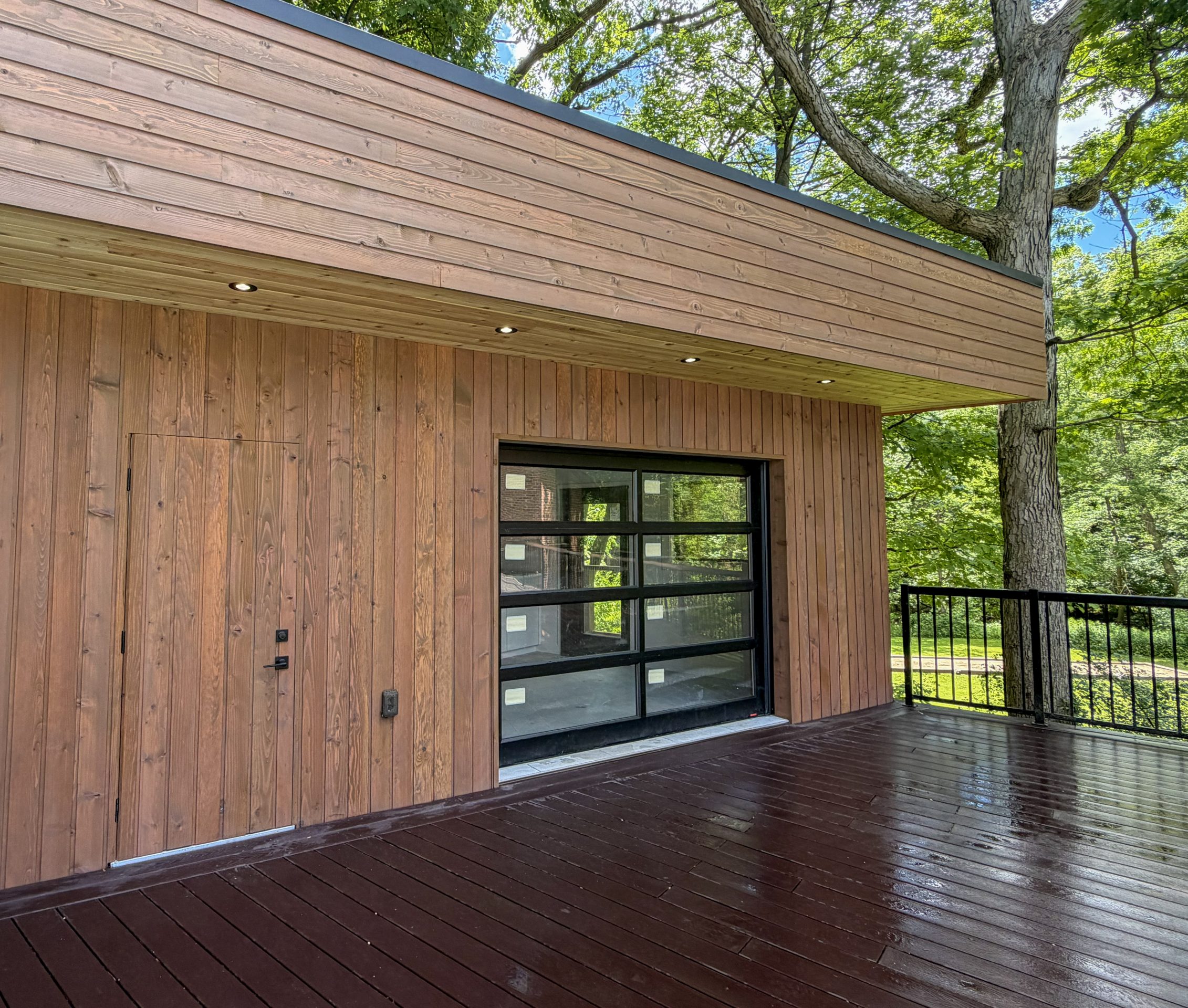 Wood siding pool house structure in a backyard with a hidden door and garage door.